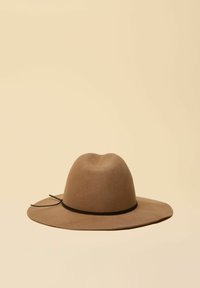 Pălărie maro cu boruri largi din fetru, cu bandă neagră și detaliu decorativ cu șnur, așezată pe un fundal bej.
