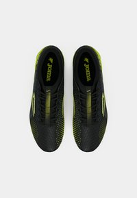 Tênis atléticos pretos e amarelos neon com parte superior texturizada, apresentando um design estampado, biqueira reforçada e a marca Joma na palmilha.