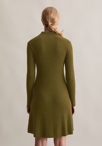 Abito in maglia a coste di color verde oliva, con maniche lunghe e gonna a campana, dotato di un colletto e tessuto testurizzato.