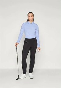 Gai zila garām piedurknēm polo krekls ar apkakli, apvienots ar melniem piegulošiem biksēm. Modelis tur golfu nūju, valkājot baltas sporta kurpes.