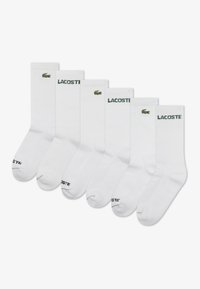 Lot de six chaussettes blanches montantes, arborant un logo crocodile vert brodé et le texte "LACOSTE" sur le bord-côte. Texture côtelée, matière en mélange de coton.