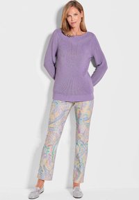 Lila gestrickter Pullover mit weitem Ausschnitt und strukturiertem Detail, kombiniert mit pastellfarbigen Hosen mit Mustern in grünen, rosa und blauen Wirbeln.