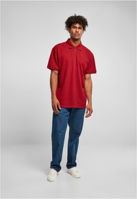 Rød polo skjorte med krage og kortermet, sammen med blå jeans og hvite joggesko. Glatt stoff, knappestolpe, avslappet passform.