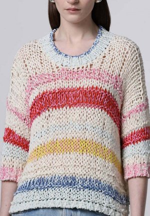 Vrouw die een losgebreide trui draagt met horizontale strepen in rood, roze, geel en blauw, met driekwart mouwen en een ronde hals.