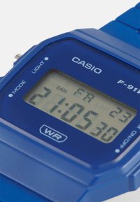 Montre numérique en plastique bleu vif avec un cadran rectangulaire, affichant l'heure et des fonctionnalités comme un chronomètre. Étiquette indiquant qu'elle est résistant à l'eau.