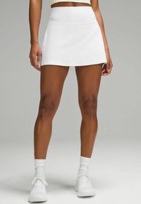 White athletic skirt with a smooth texture, mid-rise design, and a flared shape, paired with white sneakers and socks.