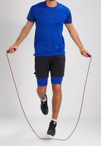 Blå atletisk t-shirt med svarta detaljer, svarta shorts, blå kompressionsshorts under och svarta sneakers medan jag använder hopprep.