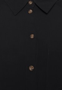 Svart skjorta med krage och bruna knappar, samt en subtilt sydd bröstficka på höger sida.