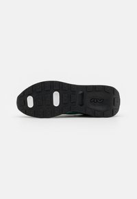 Semelle de chaussure en caoutchouc noir avec des motifs de grip texturés et des sections creuses ; elle présente une empreinte de logo et une base solide, montrant durabilité et soutien.