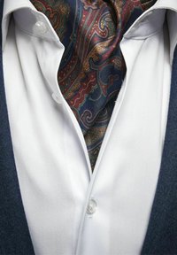 Vit skjorta med knappstängning, marinblå blazer och en mönstrad silkescarf med mörka nyanser, paisleymönster och livfulla färger.