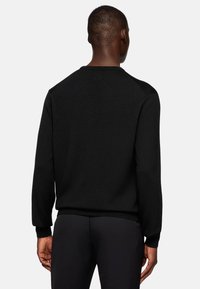 Black knitted sweater with long sleeves and a ribbed neckline. Features textured fabric and a fitted design, offering a sleek silhouette.