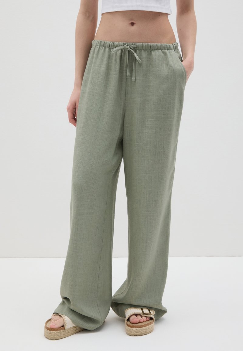 Pantalons larges vert clair en tissu texturé avec une taille élastique et un cordon de serrage, dotés de poches latérales et d'une coupe décontractée.