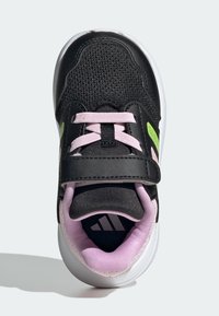 Chaussure de sport noire avec une tige en mesh, des accents roses et une bride à scratch. La semelle est blanche, avec un intérieur texturé et un logo bien visible.