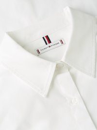 Chemise blanche à col cranté avec un bouton, présentant une étiquette Tommy Hilfiger ornée de bandes rouges, blanches et bleues sur le col. Texture lisse.