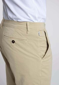 Pantalons kaki en tissu mélangé coton, avec une poche latérale, une poche arrière avec fermeture à bouton et passants de ceinture. Texture lisse et coupe ajustée.