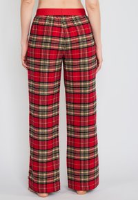 Punat ja mustad plüüšist pidžaamapüksid, millel on lai jalgade disain ja elastne vöökoht, millel on ühtlane punane äär.