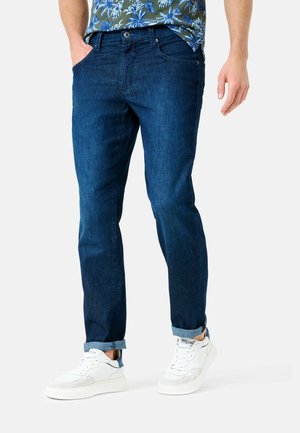 Dark blue denim jeans with a straight-cut design, featuring visible stitching and rolled cuffs. Worn with white sneakers.