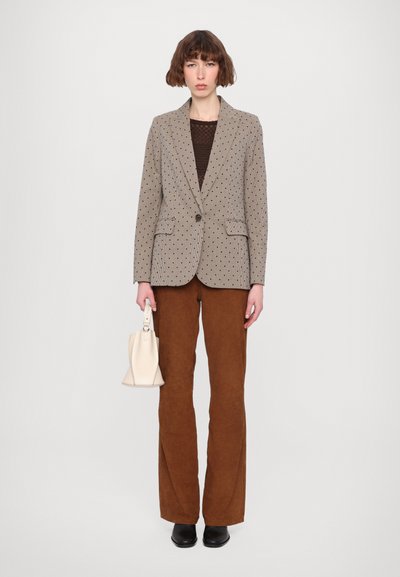 Beige mønsterjakke med blå accenter, brun strikket top, brune flagrende bukser og en cremefarvet håndtaske. Sorte sko fuldender outfittet.