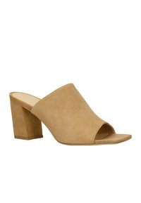Mules en suède beige à bout ouvert avec une tige large et un talon épais et carré. La semelle est plate et lisse, avec un design minimaliste.