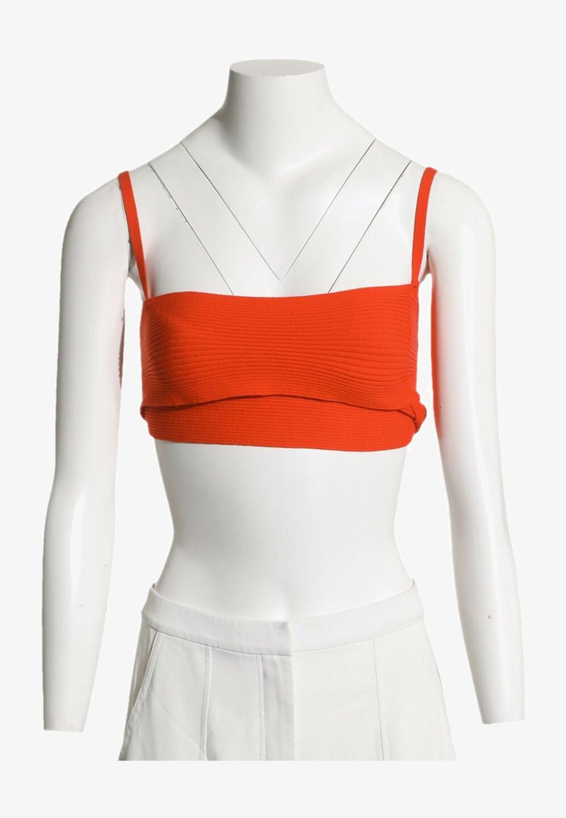 Débardeur court rouge côtelé avec fines bretelles sur buste de mannequin blanc portant un pantalon blanc.