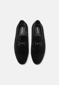 Chaussures noires en velours côtelé à enfiler avec des panneaux élastiques sur les côtés et un détail décoratif de boucle noire à l'avant. Semelle plate, tissu texturé.