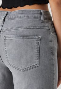 Grå denimjeans visade från baksidan, med en hög midja, två bakfickor med sömnadsdetaljer och en något sliten textur.