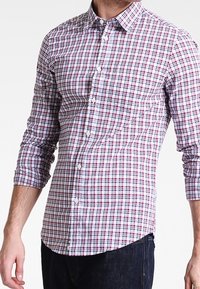 Herrskjorta med långa ärmar i vitt med ett rutigt mönster i röd och blå. Har en knappdown-krage och frontknappar, tillverkad av bomullstyg.