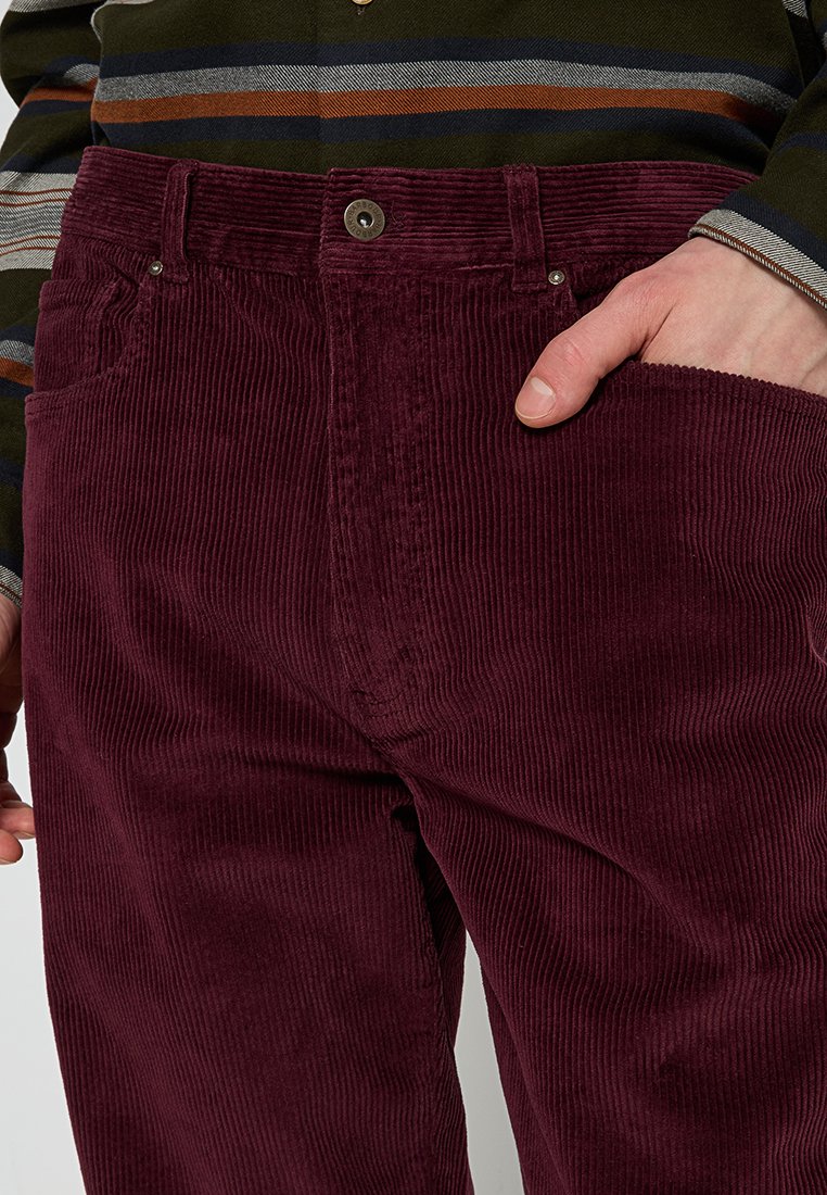 Bordowe spodnie z kordurowej tkaniny z pionowymi prążkami, z przednim zapięciem na guzik, dwiema kieszeniami i fakturowanym wykończeniem.