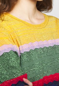 Maglione colorato a maglia con strisce orizzontali gialle, verdi e rosse, con accenti testurizzati e bordi a onde in colori contrastanti.