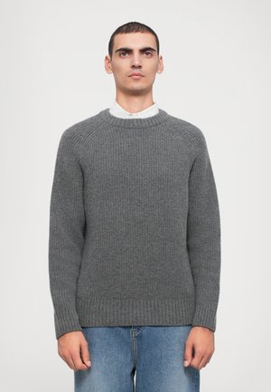 Grå strikkegenser med rund hals, ribbestrikkede ermer og hem, samt et strukturert mønster, kombinert med denimjeans.