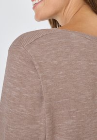 Brauner Strickpullover mit geripptem Ausschnitt und Schulternähten, der eine weiche Textur und ein dezentes meliertes Muster aufweist.