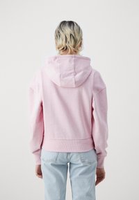 Sudadera corta rosa hecha de tela suave, con capucha y dobladillo acanalado, combinada con jeans de un azul claro.