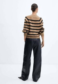 Pull en maille rayé marron avec des manches retroussées, associé à un pantalon en cuir noir ample. Fond uni.