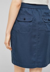 Mörkblå denimkjol med en figursydd midja, sidofickor och knapppynt. Har en slät textur och en rak kläddesign.