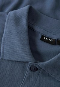 Polo blu navy con tessuto testurizzato, dotato di colletto a coste, patta con tre bottoni e etichetta nera con la scritta "LMTD."