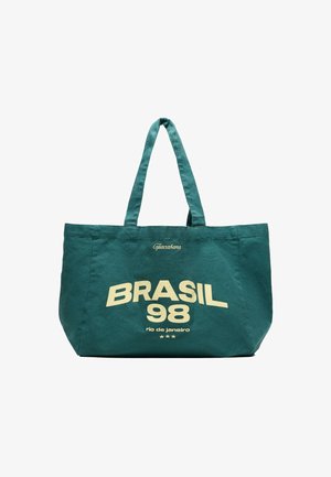 Grøn mulepose med to håndtag, gul tekst med teksten "Copacabana BRASIL 98 rio de janeiro" og tre små stjerner nedenunder.