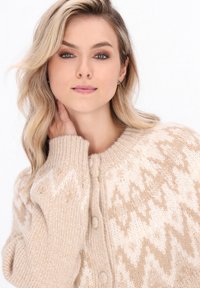 Beige gebreide cardigan met een textuur en een patroon met zigzagmotieven, een ronde hals en knoopsluiting. Zacht en comfortabel materiaal.