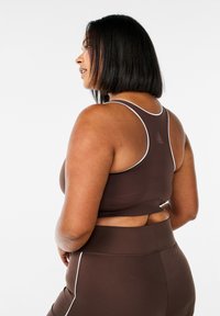 Brun sports-bh med hvid kant og racerback-design, lavet af strækbart materiale, parret med matchende høj talje leggings.