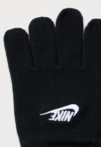 Fekete kötött kesztyű, négy ujja látható, és egy fehér Nike logó hímezve a csukló közelében.