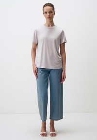Maglietta grigia chiaro a maniche corte con scollatura rotonda, abbinata a jeans azzurri larghi e tacchi bianchi aperti.