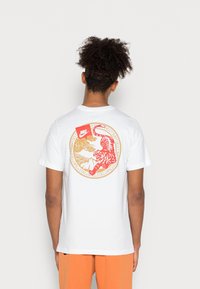 Vit bomulls t-shirt med en livfull röd tiger grafik på baksidan, omgiven av guldfärgad accent och molnmönster.