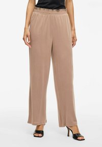 Pantalones anchos de color beige claro, fabricados con una tela suave y lisa, que cuentan con una cinturilla elástica y un corte relajado, combinados con tacones negros destalonados.