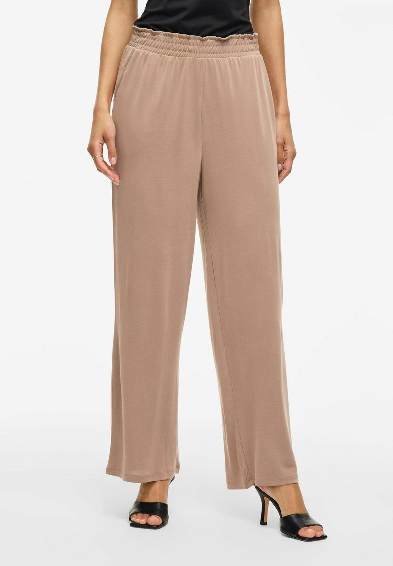 Pantalones anchos de color beige claro, fabricados con una tela suave y lisa, que cuentan con una cinturilla elástica y un corte relajado, combinados con tacones negros destalonados.