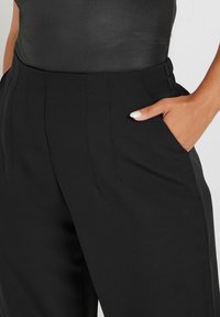 Pantalones negros a medida con una textura suave, corte recto, bolsillo lateral y detalles de costura en contraste para un aspecto sofisticado.