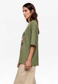 Olijfgroene oversized t-shirt met een ronde hals, korte mouwen, met een roze bloemendessin op de voorkant. Zachte textuur.