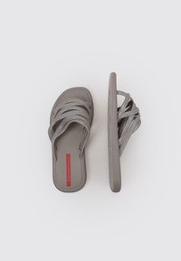 Sandalias grises con múltiples correas delgadas, una plantilla texturizada y una suela robusta. Presenta un logo rojo en la plantilla para la marca.