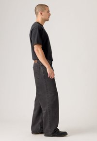 Black short-sleeve t-shirt paired with wide-leg dark gray jeans. The fabric appears soft, with a subtle texture and minimal detailing.
