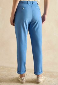Niebieskie, lekkie spodnie z elastycznym paskiem, podwiniętymi nogawkami i dwiema tylnymi kieszeniami z zapięciem na guziki. Noszone z jasnymi trampkami.