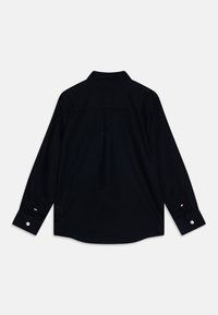 Camicia nera da uomo con bottoni e maniche lunghe, caratterizzata da una piega sul retro, un orlo arrotondato e dettagli bianchi sui polsini.