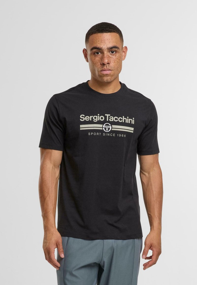 Černé bavlněné tričko s logem "Sergio Tacchini" v béžové barvě, kulatý výstřih, krátké rukávy a jednoduchý design. Nosené s šedými kalhotami.